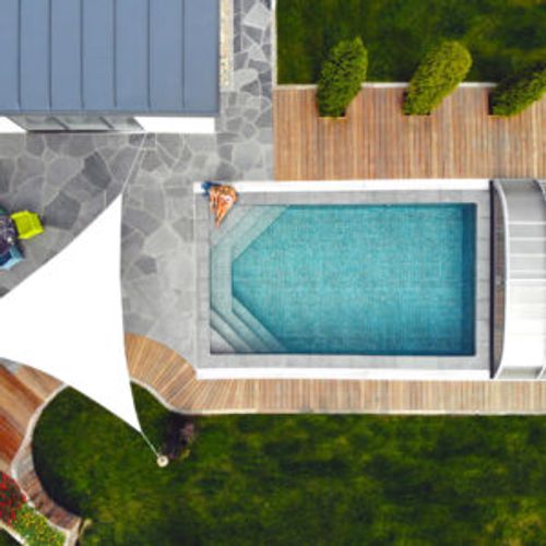 Pool rakt uppifrån med mörk mosaikliner och pooltak vid gaveln, skiffersatt stenläggning, trädäck och solsegel
