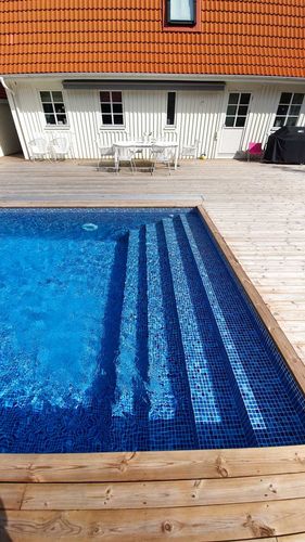 Helgaveltrappa i pool - trappsteg i blå mosaikliner som löper över hela poolens gavelbredd, med trädäck runt om