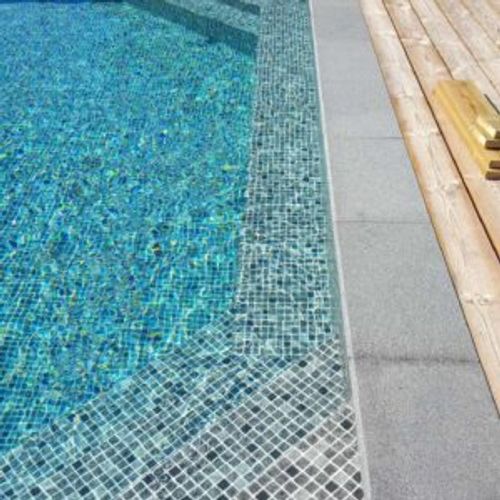 Närbild på pooltrappa i ljus mosaik mot betongsarg och trädäck